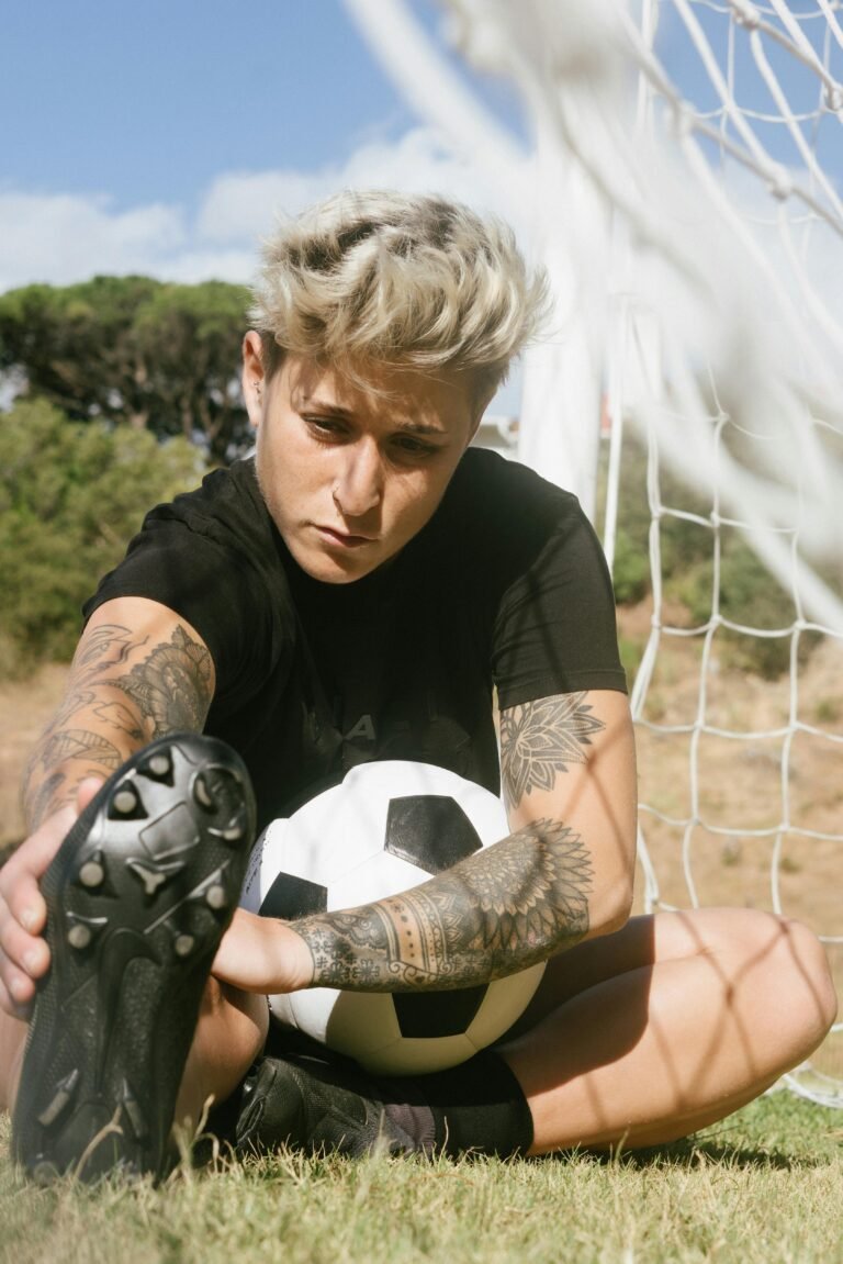 Tattooed female soccer player stretching on the field under the sun.