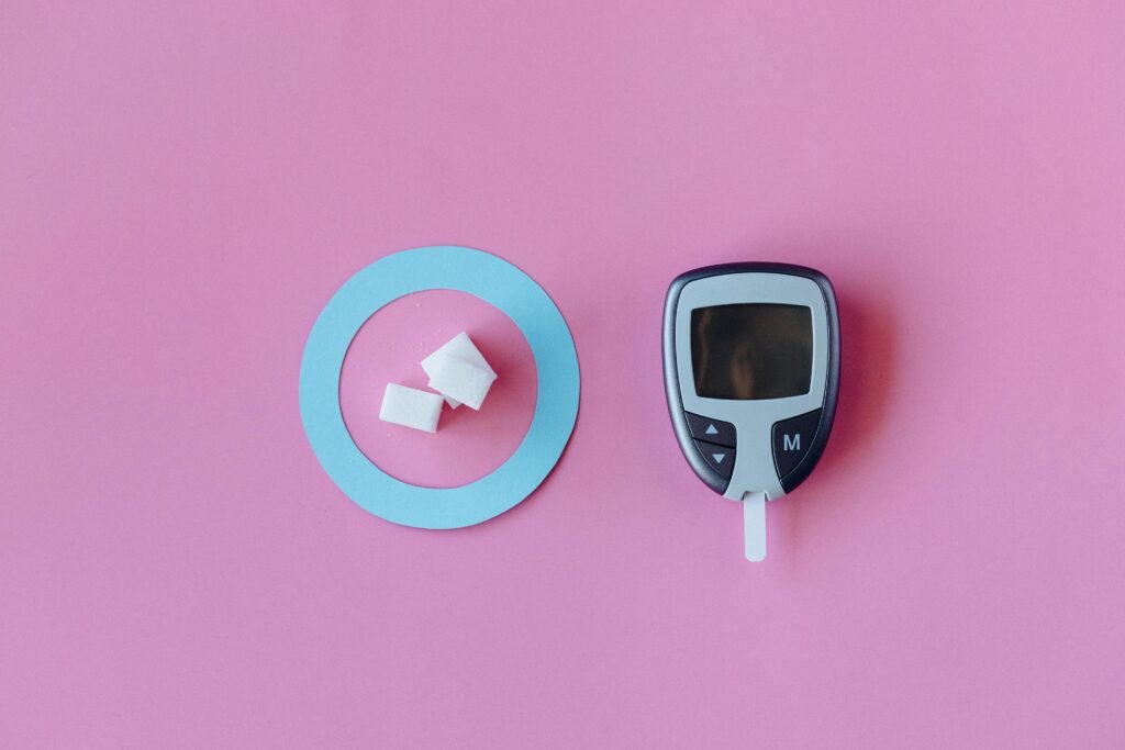 Flat lay of glucometer with sugar cubes on pink background, symbolizing diabetes awareness.