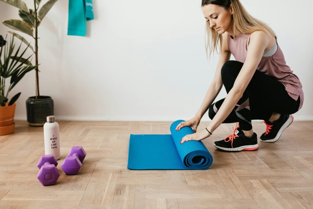 Young woman unfolding yoga mat in a home gym setting with accessories and plants.